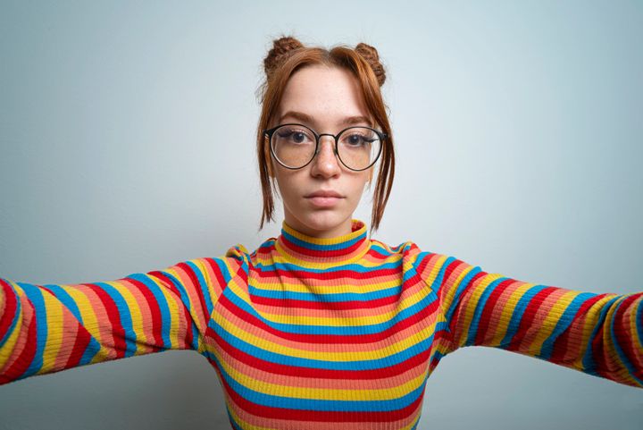 Young woman with freckles and glasses takes a selfie.Studio shot