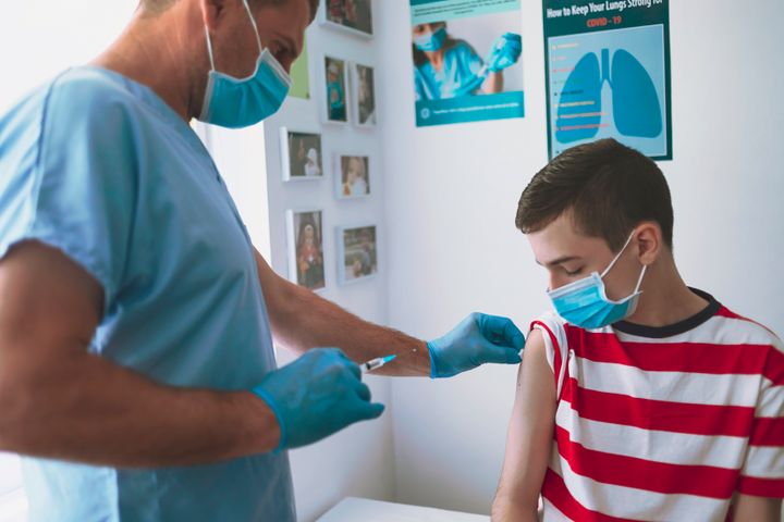 Doctor vaccinating a teenage boy. Doctor wearing protective workwear injecting vaccine into patient's arm.