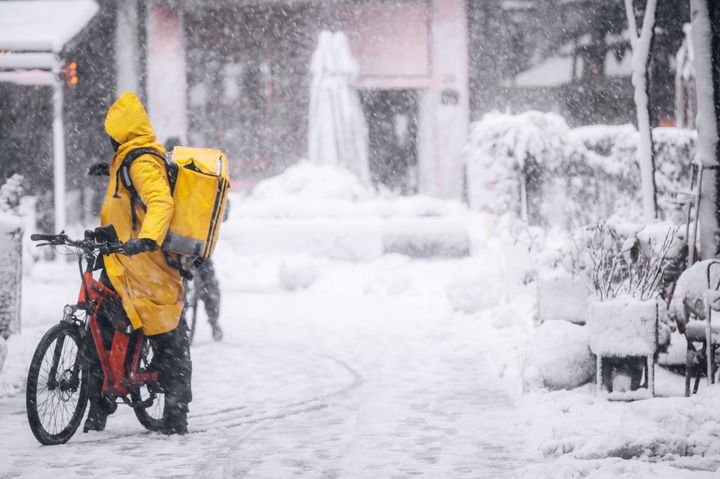 Delivery man on a bike in a snowy day, checking the right direction on a snowy day in the city center