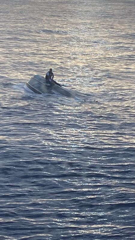 A man, who says he was one of 40 people who left Bimini, Bahamas, on Saturday before encountering severe weather, sits on a capsized boat off the coast of Fort Pierce Inlet, Florida