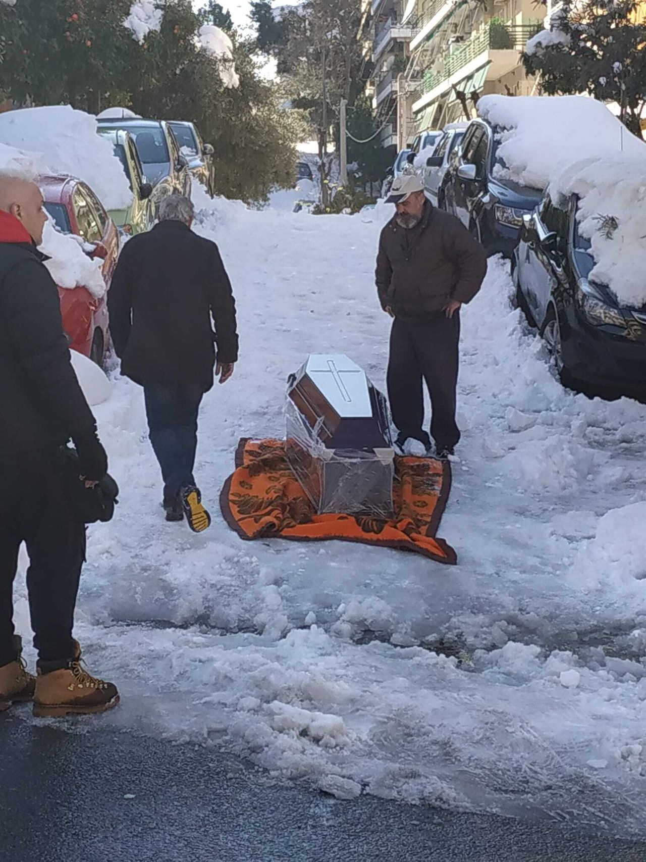 Τρεις άνδρες στου Ζωγράφου σέρνουν πάνω στο χιόνι με τη βοήθεια μιας κουβέρτας, ένα φέρετρο με σκοπό να το βάλουν στη νεκροφόρα