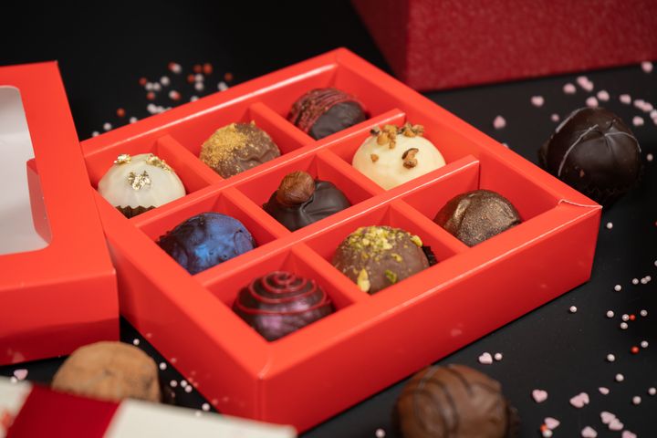 Various chocolate truffle candies in a box on gray stone background.