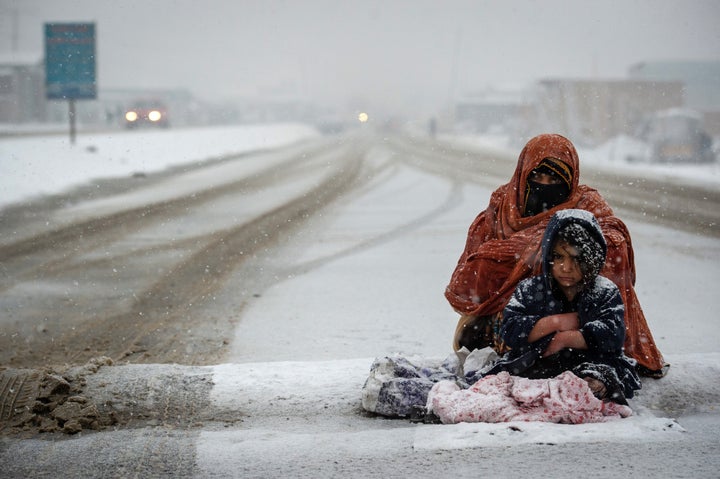 An Afghan woman, with her child huddled beside her, begs for money from passing cars on the Kabul road south to Pul-e Alam, Afghanistan.