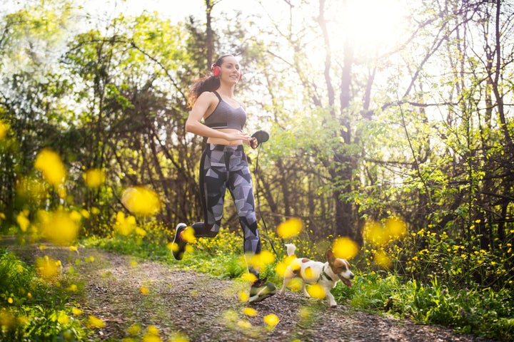 Young woman jogging in spring forest with her dog.