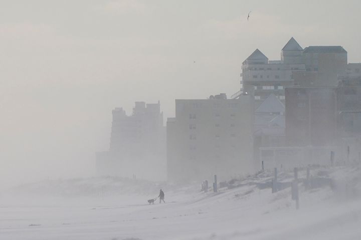 A person walks with a dog along a snow-covered beach in Ocean City, Maryland.