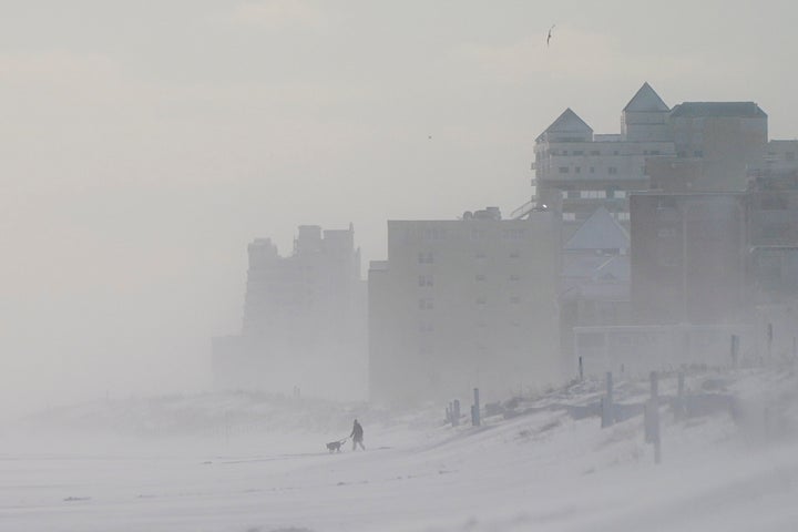 A person walks with a dog along a snow-covered beach in Ocean City, Maryland.