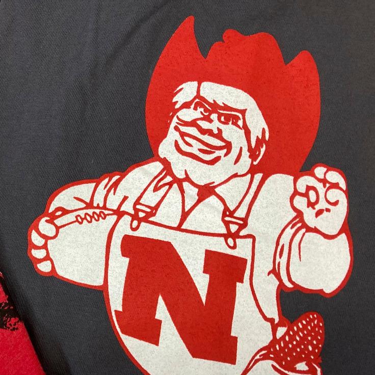 University of Nebraska T-shirts show old Herbie Husker (on the right) flashing the "OK" sign that has been adopted by white supremacists, and the new reformed Herbie flashing his new "We're No. 1" gesture.