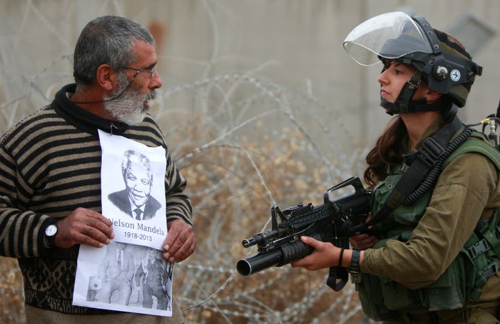 A Palestinian demonstrator holds portraits of late South African Leader Nelson Mandela and late Palestinian leader Yasser Arafat as he stands in front of Israeli soldier during a weekly demonstration against Israel's separation barrier, in the West Bank village of Bilin, near Ramallah, Dec. 6, 2013. Israel on Monday, Jan. 31, 2022, called on Amnesty International not to publish an upcoming report accusing it of apartheid, saying the conclusions of the London-based international human rights group are “false, biased and antisemitic.”