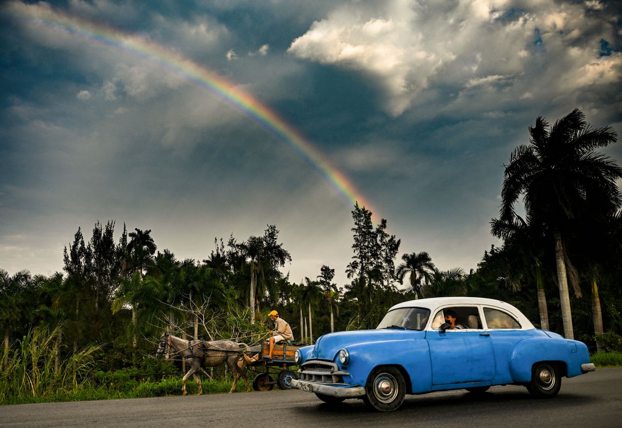 A 1949 Chevy keeps up with a mule cart in Havana as a rainbow appears behind them Thursday.