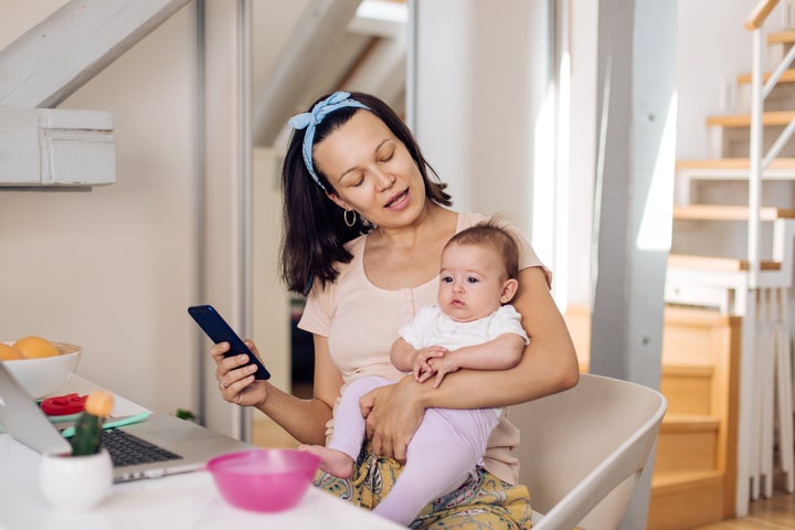 A woman holding a baby and operating a laptop