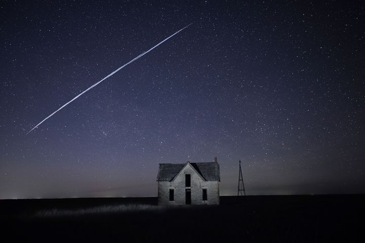 Μια σειρά από δορυφόρους SpaceX StarLink του Έλον Μασκ περνάει πάνω από ένα παλιό πέτρινο σπίτι.