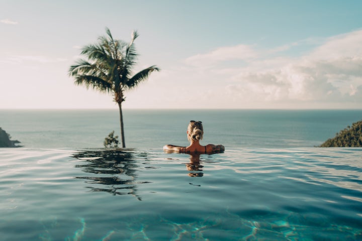 Rear view of a woman standing leaned at the edge of a pool and enjoying the amazing sea view.