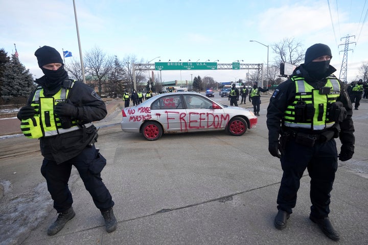 Police look on as a protest vehicle leaves a demonstration which has blocked traffic across the Ambassador Bridge by protesters against COVID-19 restrictions in Windsor, Ont., Saturday, Feb. 12, 2022. Canadian police have moved in to remove protesters who have disrupted Canada-U.S. trade at the major bridge border crossing. (Nathan Denette/The Canadian Press via AP)