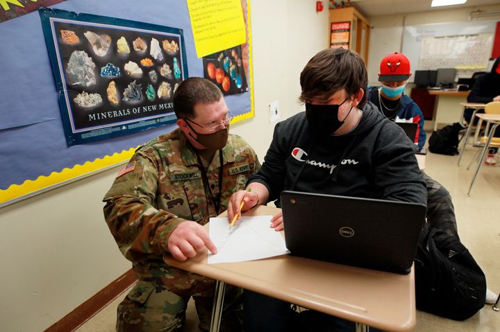 New Mexico Army National Guard specialist Michael Stockwell kneels while helping Alamogordo High School freshman Aiden Cruz with a geology assignment, at Alamogordo High School,Tuesday, Feb. 8, 2022, in Alamogordo, N.M. 