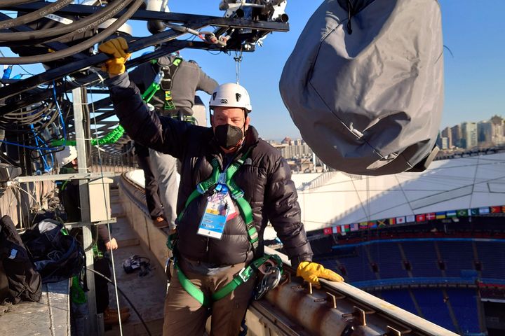 Ο φωτογράφος του Associated Press, Κρις Κάρλσον, ποζάρει για μια φωτογραφία ενώ εγκαθιστά μια απομακρυσμένη κάμερα στην οροφή του Εθνικού Σταδίου, γνωστής ως η Φωλιά του Πουλιού, στο Πεκίνο, στις 28 Ιανουαρίου 2022. (AP Photo/David J. Phillip)
