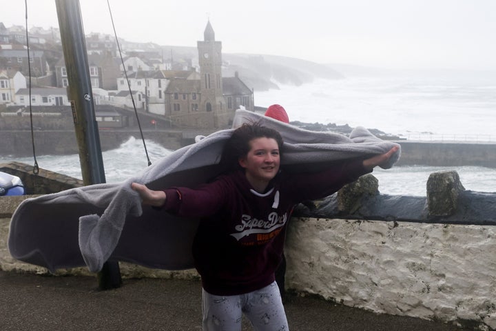 A person covers herself as large waves and strong winds hit during Storm Eunice, in Cornwall.