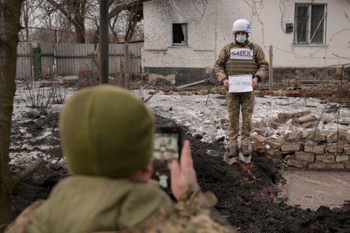 Members of the Joint Centre for Control and Coordination on ceasefire of the demarcation line take forensic photos of a crater and damage to a house from an artillery shell that landed in Vrubivka, one of at least eight that hit the village in the Luhansk region of eastern Ukraine, Thursday, Feb. 17, 2022. (AP Photo/Vadim Ghirda)