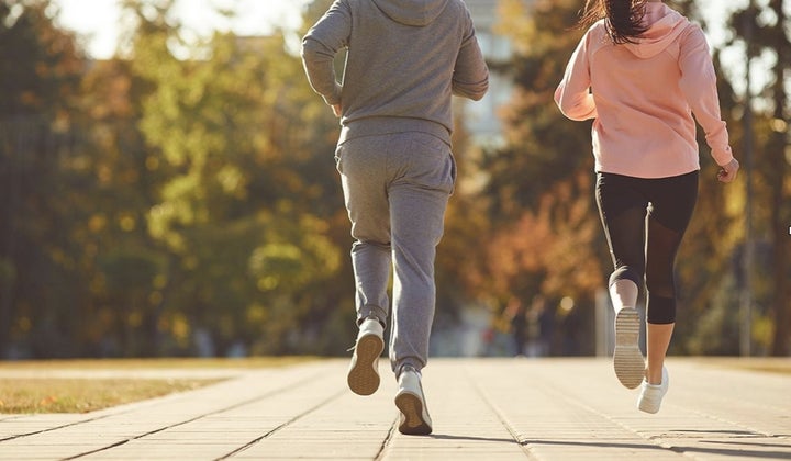 A man and a woman are running along the city street in the morning.