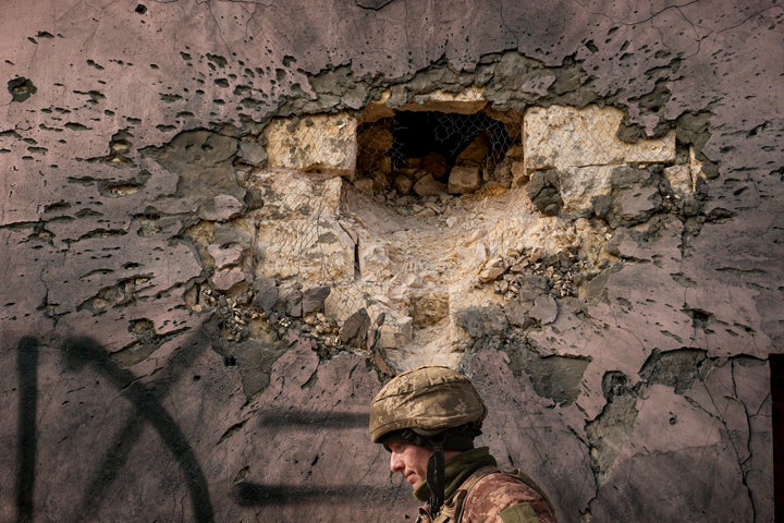 A Ukrainian serviceman walks by a building which was hit by a large caliber mortar shell in the frontline village of Krymske, Luhansk region, in eastern Ukraine, Saturday, Feb. 19, 2022.