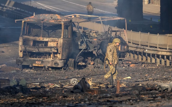 A Ukrainian soldier walks past debris of a burning military truck, on a street in Kyiv, Ukraine, Saturday, Feb. 26, 2022. Russian troops stormed toward Ukraine's capital Saturday, and street fighting broke out as city officials urged residents to take shelter. (AP Photo/Efrem Lukatsky)