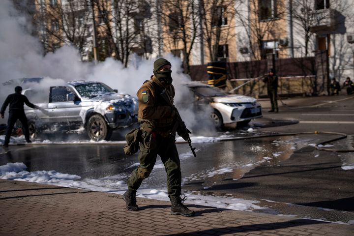 Ukrainian soldiers take positions outside a military facility as two cars burn, in a street in Kyiv, Ukraine, Saturday, Feb. 26, 2022. (AP Photo/Emilio Morenatti)