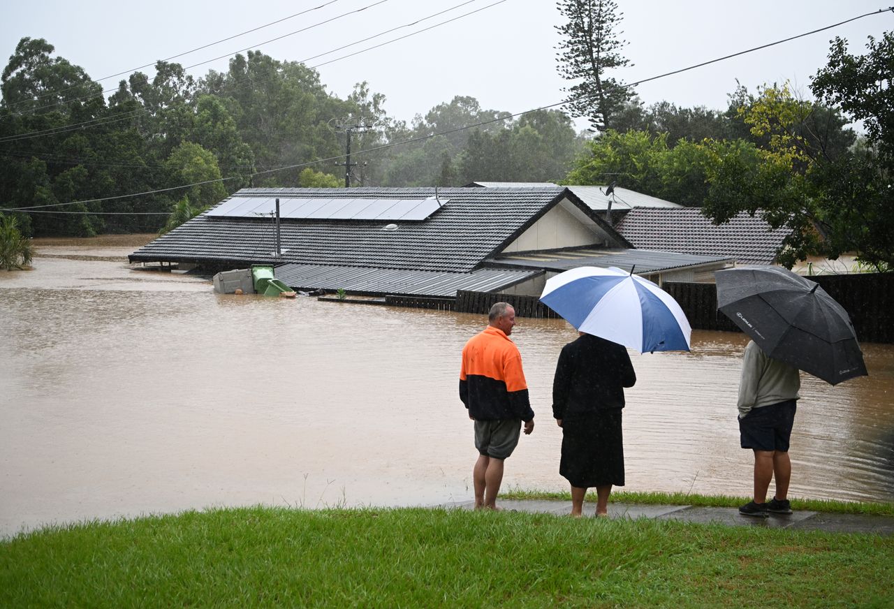 People look on as a house is inundated by flood water on February 27, 2022, in Goodna, west of Brisbane, Australia.