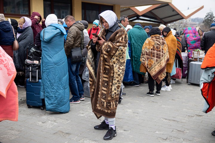 A lady wrapped in a blanket and using her phone while waiting for the train to go back to Ukraine at Przemysl train station. 