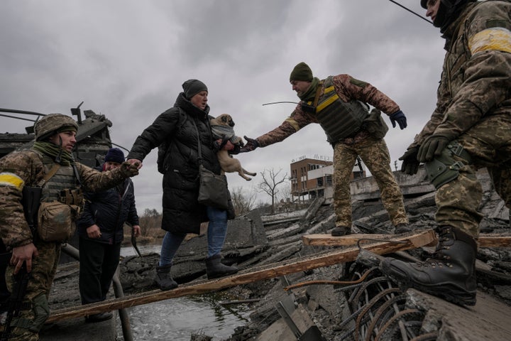 Ukrainian servicemen help a woman carrying a small dog across the Irpin River on an improvised path while assisting people fleeing the town on Saturday.