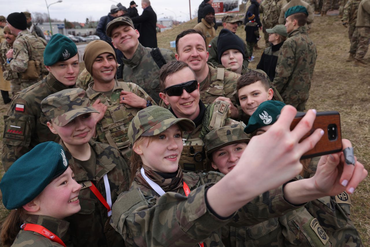A member of the youth group of Poland's Territorial Defense Force takes a selfie with soldiers of the U.S. Army's 82nd Airborne Division, who are stationed at a nearby airfield, during a local commemorative run in the town center on Sunday near Mielec, Poland.