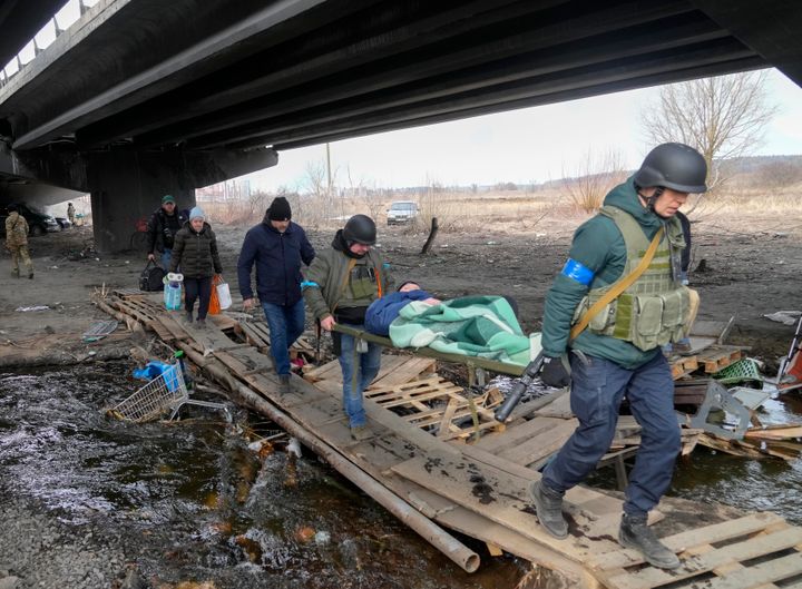 Ukrainians soldiers pass an improvised path under a destroyed bridge as they evacuate an elderly resident in Irpin, northwest of Kyiv, Saturday, March 12, 2022. (AP Photo/Efrem Lukatsky)