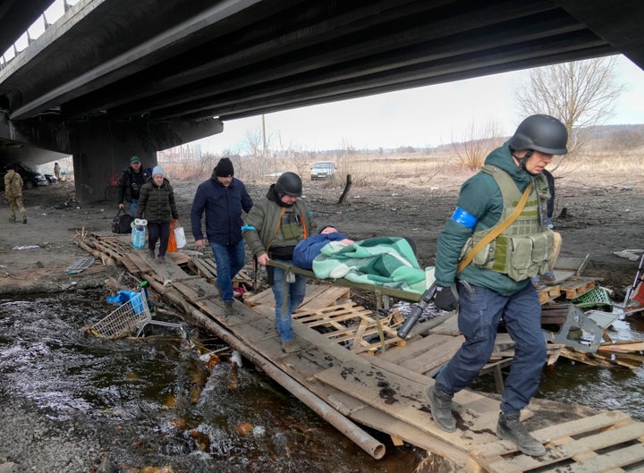 Ukrainians soldiers pass an improvised path under a destroyed bridge as they evacuate an elderly resident in Irpin, northwest of Kyiv, Saturday, March 12, 2022. (AP Photo/Efrem Lukatsky)