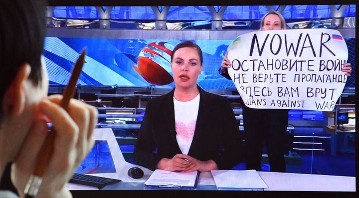 A woman looks at a computer screen watching a dissenting Russian Channel One employee entering an on-air TV studio during Russia's most-watched evening news broadcast, holding up a poster that reads "No War" and condemning Moscow's military action in Ukraine.