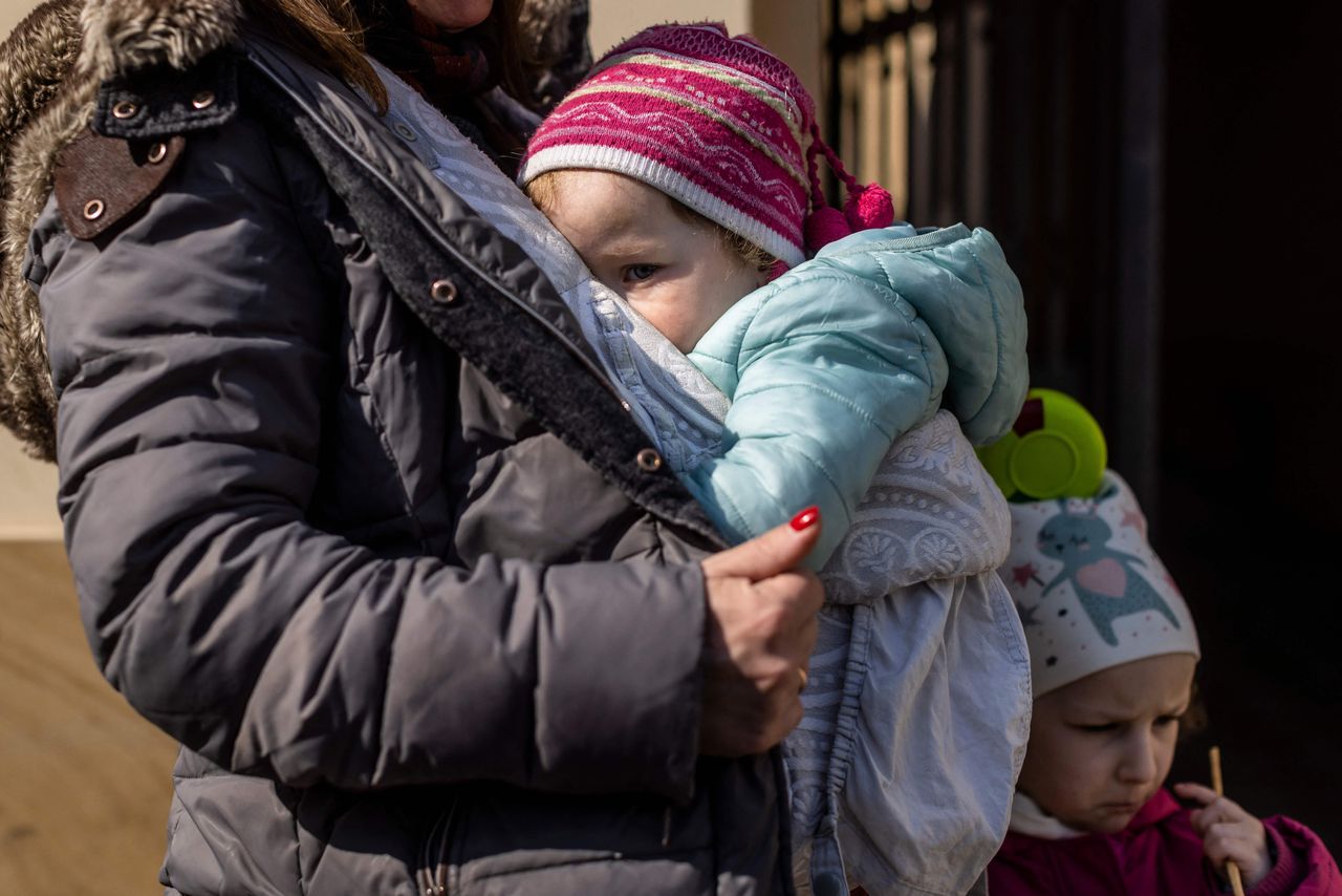 A woman from Ukraine holds her baby in front of the railway station in Przemysl as she and other refugees prepare to board a free bus which will take them to Germany.