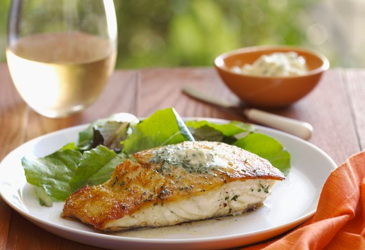 A healthy entree of Halibut fish served with salad and white wine in an outdoor setting.