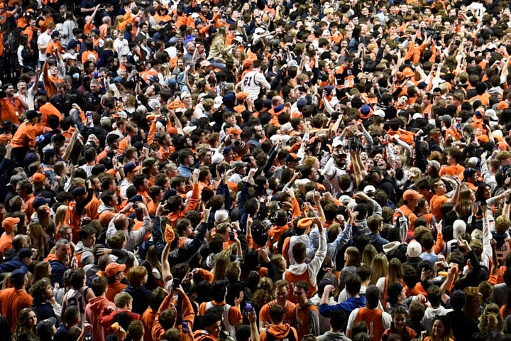 FILE - Fans storm the court at the conclusion of a college basketball game in Champaign, Ill., on Sunday, March 6, 2022. After about two months of falling COVID-19 cases, pandemic restrictions have been lifted across the U.S., and many people are taking off their masks and returning to indoor spaces. (AP Photo/Michael Allio)