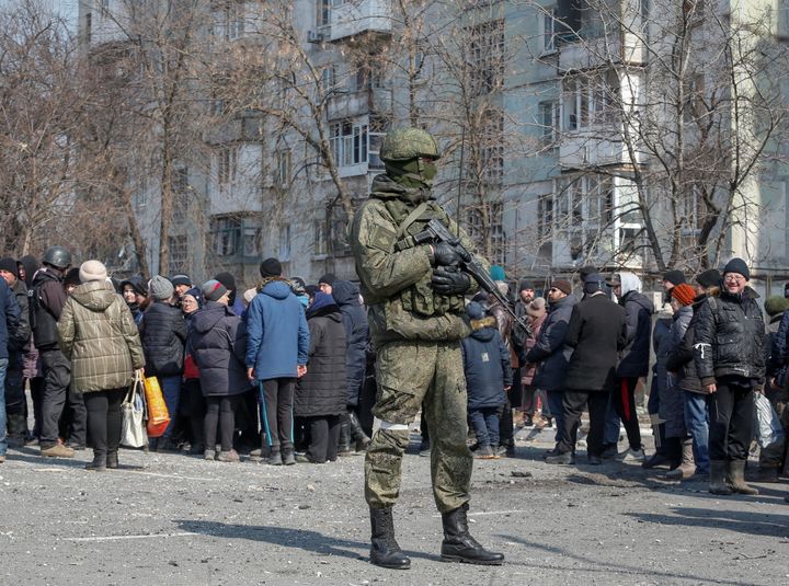 Ένας Ρώσος στρατιώτης στέκεται δίπλα σε ντόπιους που περιμένουν στην ουρά για ανθρωπιστική βοήθεια που παραδόθηκε κατά τη διάρκεια της σύγκρουσης Ουκρανίας-Ρωσίας, στο πολιορκημένο νότιο λιμάνι της Μαριούπολης, Ουκρανία, 23 Μαρτίου 2022.