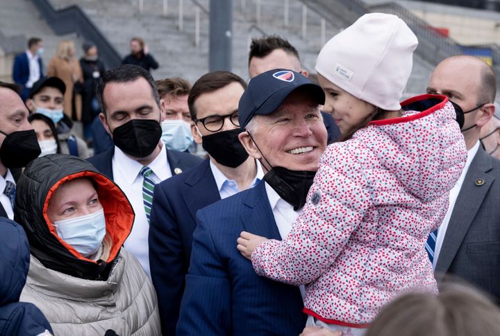 US President Joe Biden (R) holds a girl on his arm as he and Polish Prime Minister Mateusz Morawiecki (C) meet with Ukrainian refugees at PGE Narodowy Stadium in Warsaw on March 26, 2022.