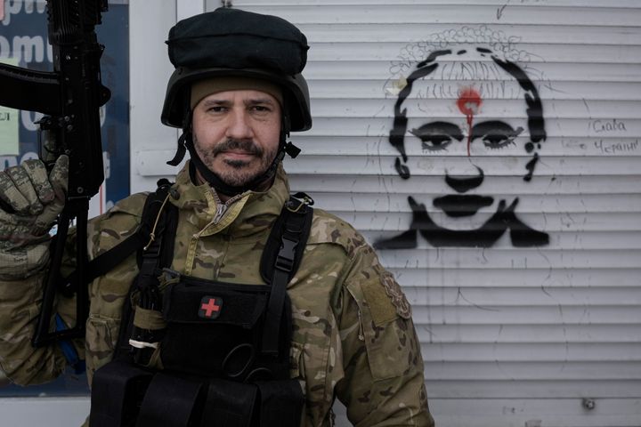 A Ukrainian serviceman poses next to a graffiti depicting Russian President Vladimir Putin and the words 'Glory to Ukraine" on the blinds of a battle damaged shop in Stoyanka, Ukraine, Sunday, March 27, 2022. Ukrainian President Volodymyr Zelenskyy accused the West of lacking courage as his country fights to stave off Russia's invading troops, making an exasperated plea for fighter jets and tanks to sustain a defense in a conflict that has ground into a war of attrition.