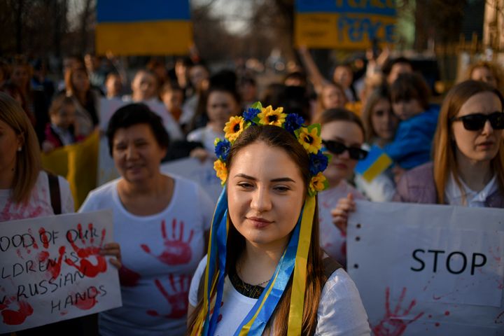 Μια γυναίκα που φορά ένα στέμμα λουλουδιών με μπλε και κίτρινες κορδέλες, στο χρώμα της ουκρανικής σημαίας, ακούει τον εθνικό ύμνο της Ουκρανίας κατά τη διάρκεια διαμαρτυρίας κατά του πολέμου της Ρωσίας στην Ουκρανία, μπροστά από τη ρωσική πρεσβεία στο Βουκουρέστι, Ρουμανία, Κυριακή 27 Μαρτίου, 2022.