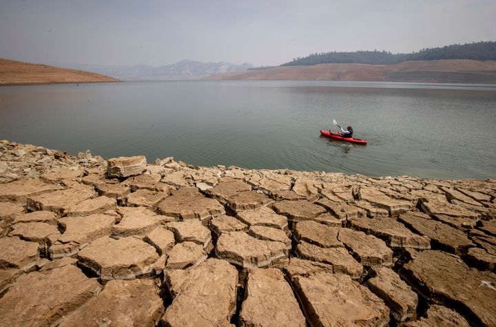 A kayaker fishes in Lake Oroville, in California, in August 2021 under a smoke-filled sky. A years-long drought has caused the reservoir to dry up. (AP Photo/Ethan Swope, File)