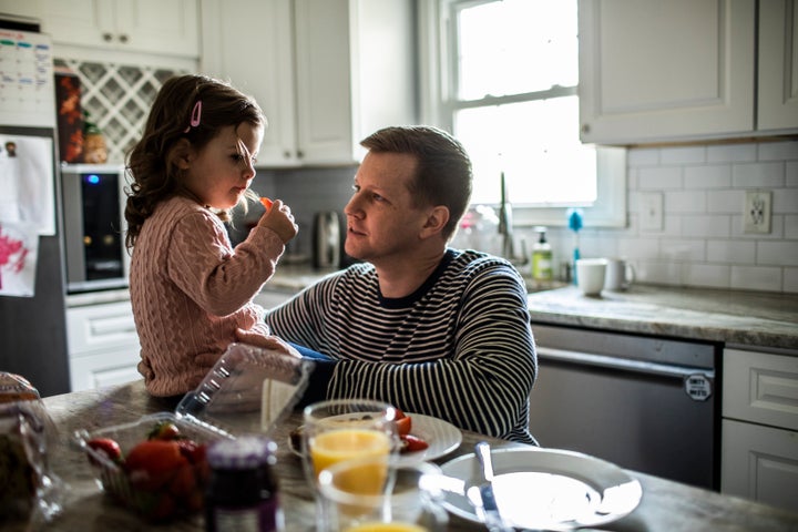 Toddler girl feeding her father a strawberry in kitchen