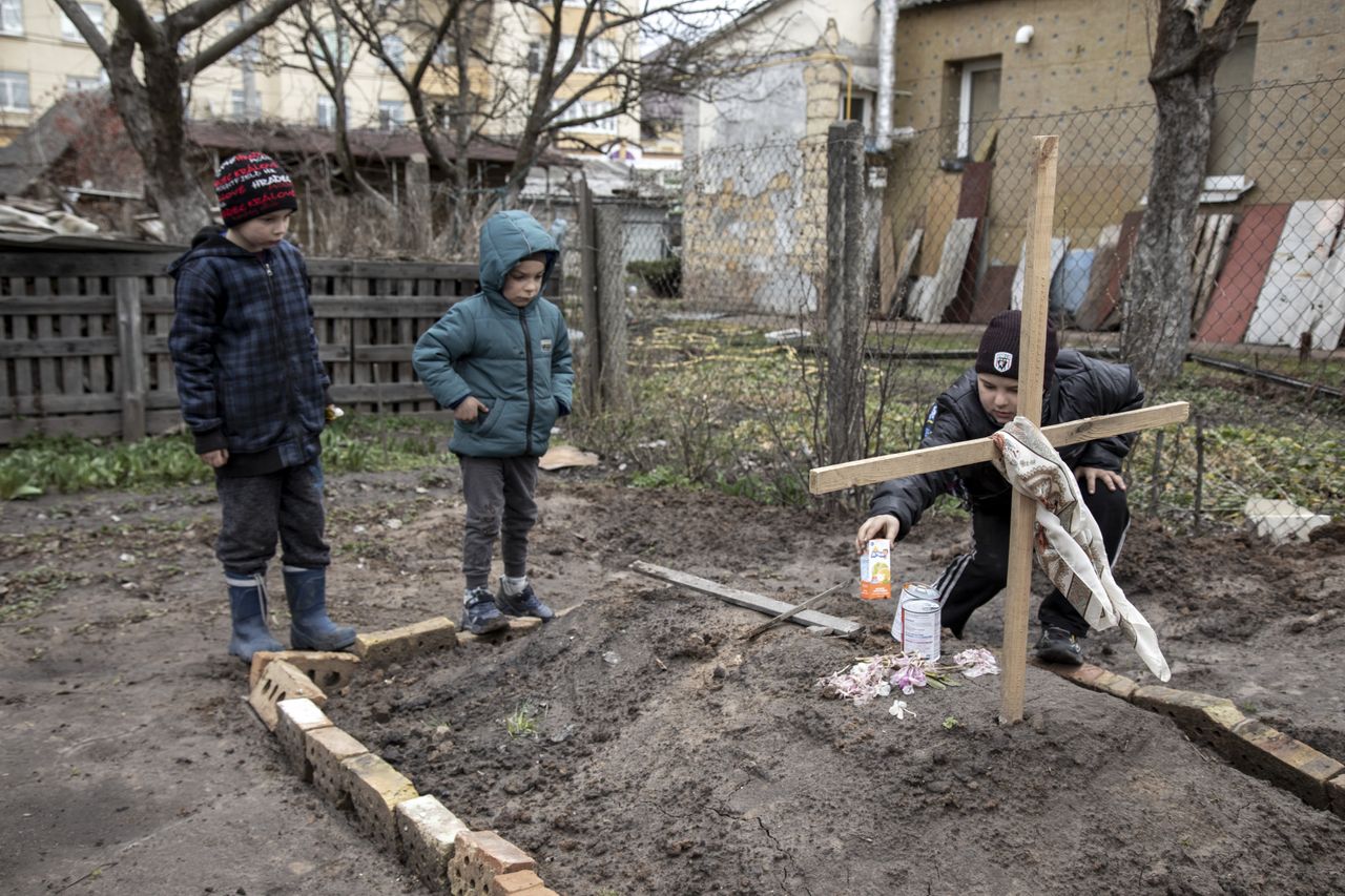 A young child gives an offering of food to his mother's grave as his younger brother and a neighbour stand next to it, in the town of Bucha, on the outskirts of Kyiv.