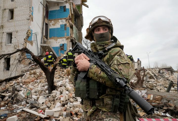 A Ukrainian soldier stands outside of a building destroyed by Russian shelling