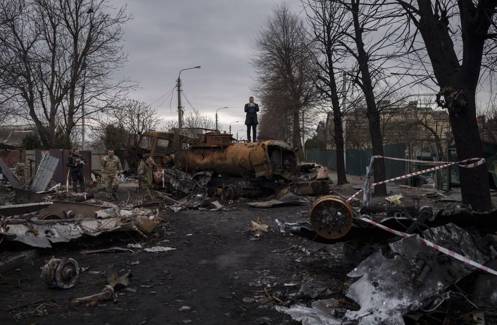 Δημοσιογράφος στέκεται πάνω σε κατεστραμμένο όχημα, μετά από μάχες ρωσικών και ουκρανικών δυνάμεων, στην Μπούτσα.