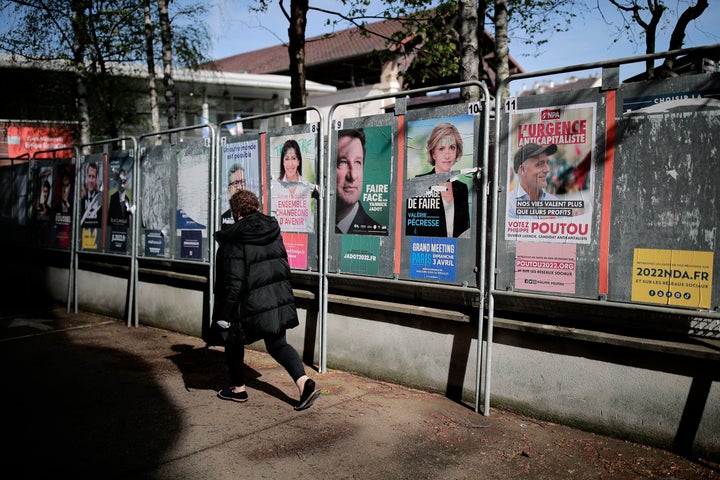 A woman walks past presidential campaign posters during the first round of the French presidential election in Saint-Denis, outside Paris, Sunday, April 10, 2022. (AP Photo/Lewis Joly)