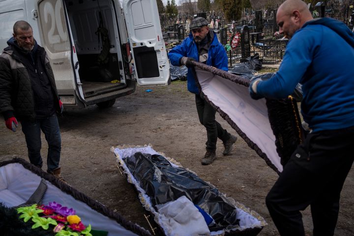 Cemetery workers prepare the coffin for a person killed during the war with Russia, as dozens of black bags containing more bodies of victims are seen strewn across the graveyard in the cemetery in Bucha, in the outskirts of Kyiv, Ukraine, Monday, April 11, 2022. (AP Photo/Rodrigo Abd)