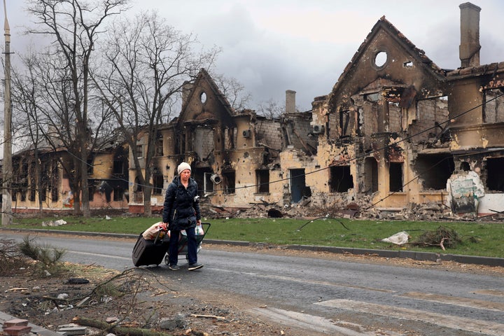 A woman pulls her bags past houses damaged during fighting in eastern Mariupol, Ukraine.