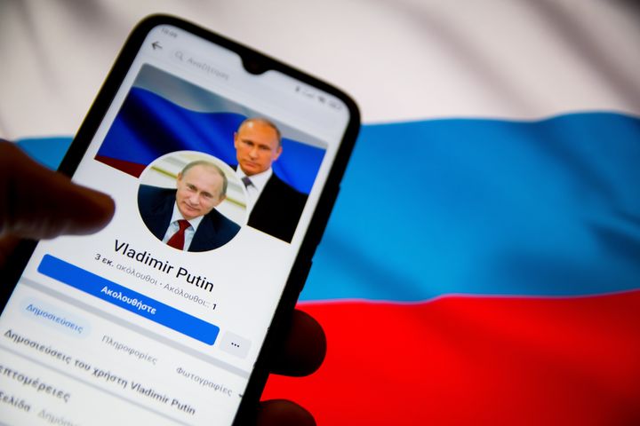 In this photo illustration Vladimir Putin Facebook page seen displayed on a smartphone screen with a flag of Ukraine on computer screen in the background in Athens, Greece on February 25, 2022. (Photo illustration by Nikolas Kokovlis/NurPhoto via Getty Images)