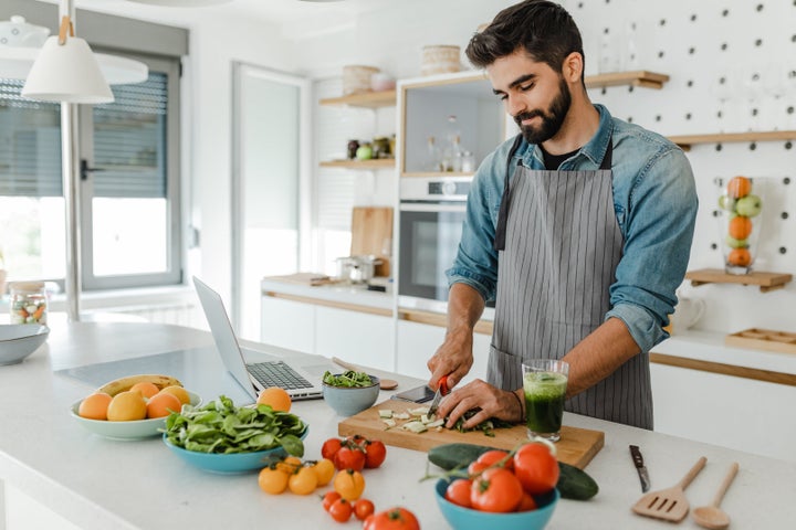 A young handsome man is in the kitchen, he is chopping food and preparing a meal