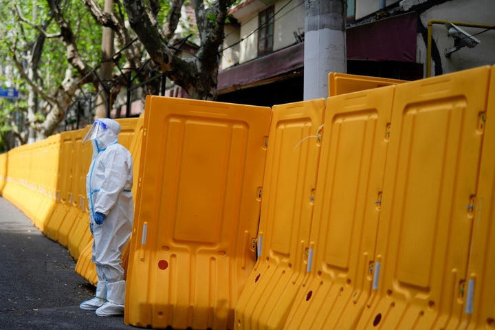 A worker in a protective suit keeps watch at barriers sealing off an area under lockdown amid the coronavirus disease (COVID-19) pandemic, in Shanghai, China April 15, 2022.